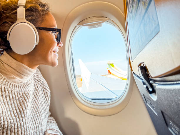 A woman enjoys her flight while wearing noise-canceling headphones, gazing out of the airplane window.